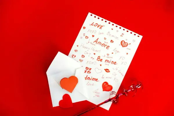 Une feuille blanche ornée de mots d'amour et de cœurs rouges, sortant d'une enveloppe. Un texte touchant pour son parrain.
