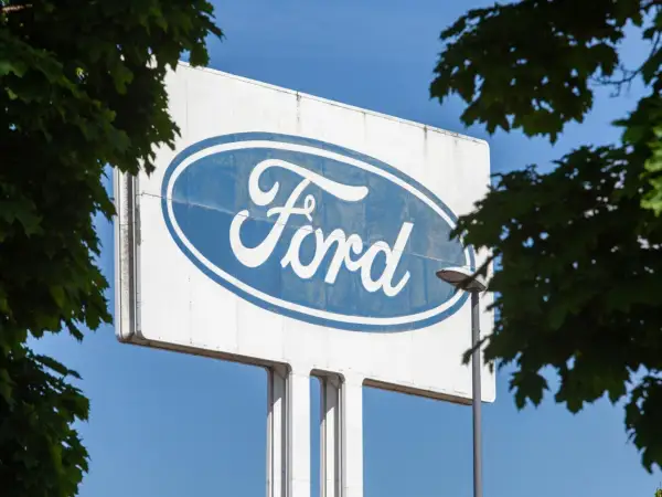 Großes Ford-Logo auf einem Schild, umgeben von grünen Blättern. Vielleicht ein Zeichen für eine neue Ära oder eine ford abfindung.