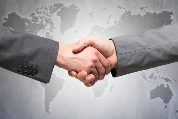Uścisk dłoni dwóch mężczyzn w garniturach na tle mapy świata. Symbolizuje globalne partnerstwo i ddp.