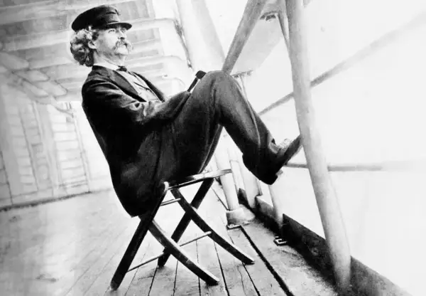 Mark Twain sitter på en stol på ett skeppsdäck, med en hatt och en mustasch. En bild som inspirerar till ett mark twain citat om livet.