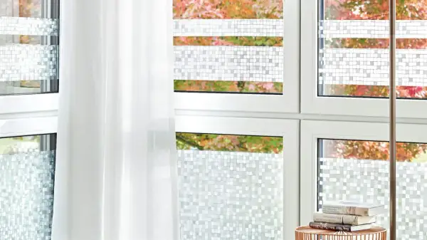 Fenster mit statischer Fensterfolie im Mosaikmuster, die Privatsphäre schafft. Ein weißer Vorhang hängt daneben.