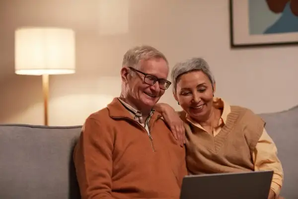 Uśmiechnięta para seniorów przegląda coś na laptopie. Może planują urlop bezpłatny, by cieszyć się emeryturą.
