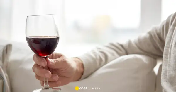 Dłoń trzyma kieliszek czerwonego wina. Czy czerwone wino obniża ciśnienie? Warto to sprawdzić.