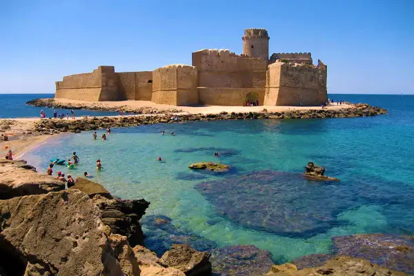 Castello Aragonese su un'isola con mare cristallino, bagnanti e rocce. Un vero spettacolo del **calabria mare bello**.