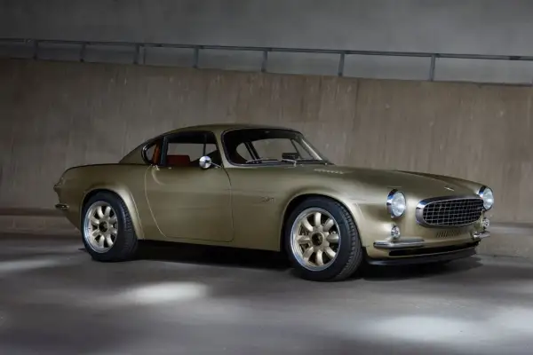 En gyllene Volvo P1800, en tidlös klassiker med en modern touch, står parkerad mot en betongvägg.