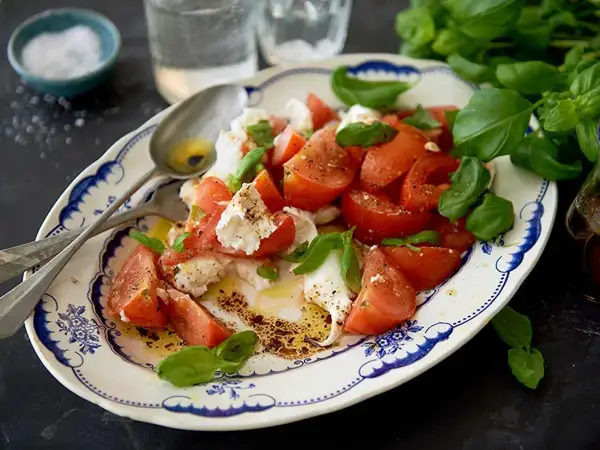 En härlig caprese sallad med saftiga tomater, krämig mozzarella och färsk basilika, ringlad med olivolja och balsamvinäger.