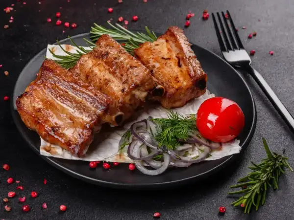 Soczyste żeberka z grilla, podane z pomidorkiem, cebulką i ziołami. Idealne na letnie wieczory.