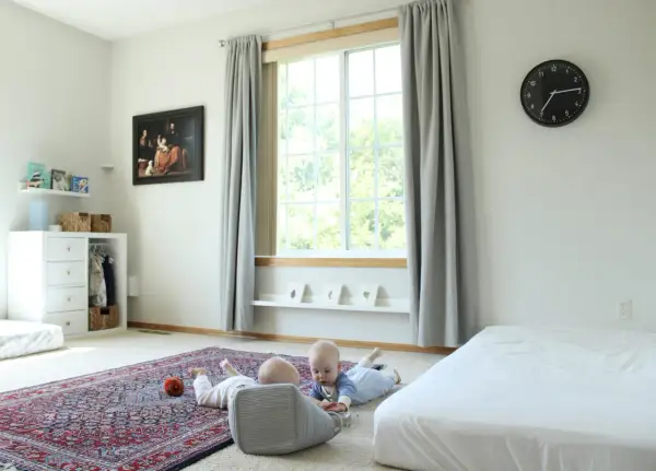 Two babies explore a room with a Montessori inspired feel, featuring a rug, toy basket, and artwork.