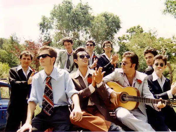 Grupo de hombres con trajes, uno toca la guitarra, listos para una rumba catalana bajo el sol.
