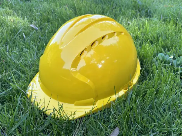 Żółty kask ochronny leży na trawie. Pamiętaj o sprawdzeniu **daty ważności kasku ochronnego** przed użyciem.