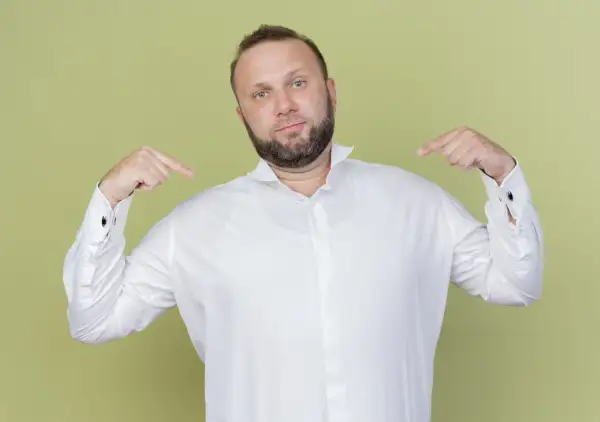 Mann zeigt auf sich und sein weißes Hemd. Er fragt sich, welches Unterhemd unter dem Hemd am besten passt.