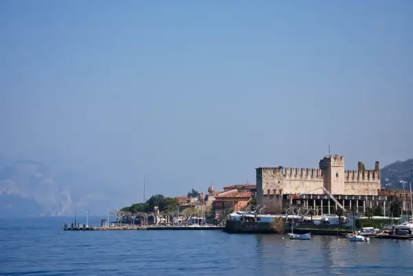 Rocchetta di Moniga del Garda, un gioiello da vedere sul lago. Passeggiata sul lungolago con barche e montagne sullo sfondo.