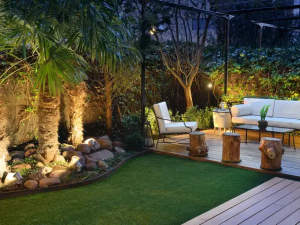 Jardines pequeños y sencillos con palmeras iluminadas, césped artificial y mobiliario de exterior.
