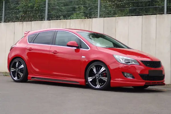 Czerwony Opel Astra J z przyciemnianymi szybami i efektownymi felgami. Widać jego światła pozycyjne.
