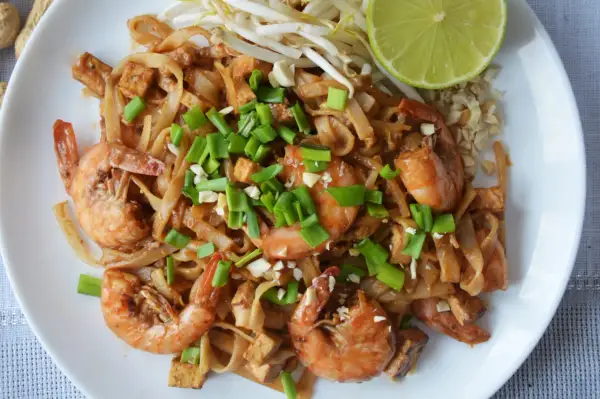 Pyszny pad thai kung z krewetkami, tofu i szczypiorkiem, podany z kiełkami fasoli mung i ćwiartką limonki.