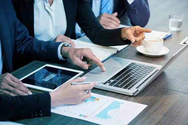 Persone in abiti eleganti collaborano a un tavolo, analizzando dati su tablet e laptop. Sono le risorse umane che lavorano insieme per il successo.