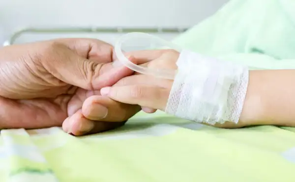 Dłoń rodzica trzyma dłoń dziecka w szpitalu, gdzie wystawiane jest zwolnienie na dziecko w szpitalu.