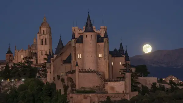 El majestuoso castillo de Segovia se alza bajo una luna llena, con su imponente arquitectura y torres que parecen vigilar la noche.