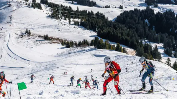 Skibergsteigen-Athleten kämpfen sich einen verschneiten Hang hinauf, bereit für olympische Herausforderungen.