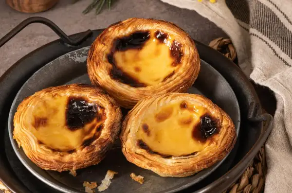 Trzy pyszne portugalskie ciastka, znane jako pastéis de nata, z chrupiącym ciastem i kremowym, lekko przypieczonym nadzieniem.