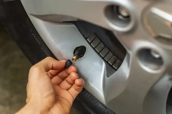 Main d'une personne retirant le capuchon d'un valve pneu qui fuit, révélant le mécanisme de la valve.