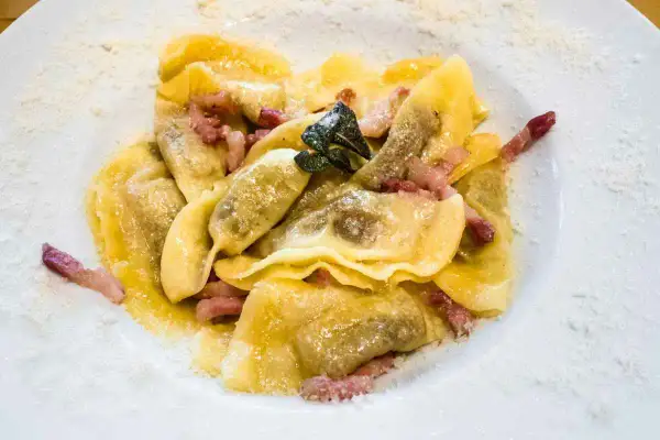 Deliziosi ravioli bresciani conditi con pancetta croccante e una foglia di salvia, spolverati di parmigiano.
