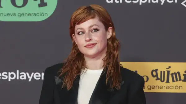 Chloe Wallace, con su cabello pelirrojo y mirada cautivadora, posa con un blazer negro.