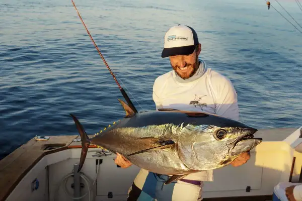 Glücklicher Angler hält stolz einen riesigen Thunfisch, den er beim Thunfisch angeln gefangen hat. Das Boot schaukelt sanft auf dem Meer.