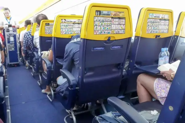 Wnętrze samolotu Boeing 737 Ryanair. Pasażerowie siedzą w rzędach, na oparciach foteli widoczne są instrukcje bezpieczeństwa.