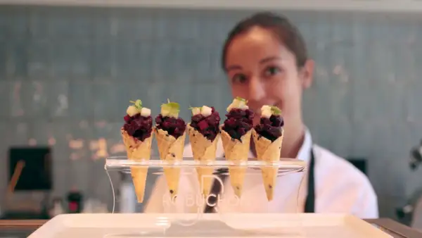 Cinco conos de gofre con tartar de remolacha y cubitos de manzana, presentados en un soporte con el logo Robuchon.
