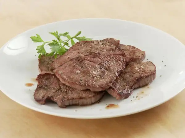 Saftiges Schnitzel Natur, gewürzt mit Pfeffer und Salz, auf einem weißen Teller mit Petersilie garniert.