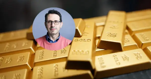 Mężczyzna w okularach na tle sztabek złota. Czy złoto traci na wartości? Analiza eksperta.