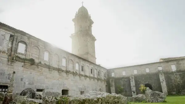 El imponente **monasterio de Oia** se alza bajo un cielo brumoso, con su torre campanario y sus muros de piedra evocando historias de siglos pasados.