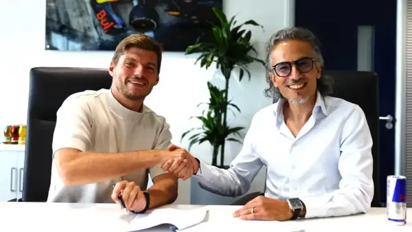 Max Verstappen sonríe mientras estrecha la mano de un hombre con gafas, sellando un acuerdo.