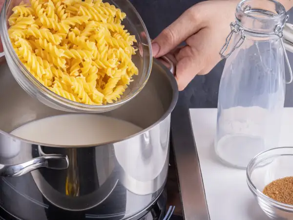 Eine Hand schüttet Spiralnudeln in einen Topf mit Milch. Zutaten für milch nudeln.