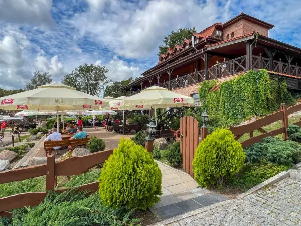 Odkryj najlepsze restauracje na Mazurach! Letni ogródek z widokiem na jezioro, gdzie można delektować się posiłkiem pod parasolami.