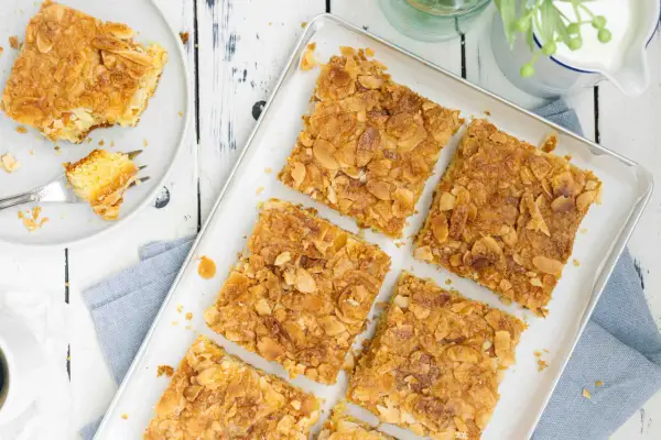 Saftiger butterkuchen ohne hefe, bestreut mit knusprigen Mandelblättchen. Ein Stück auf einem Teller mit einer Gabel.