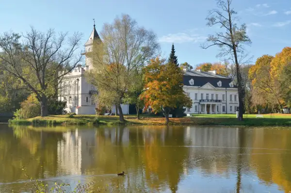 Pałac w jesiennej scenerii nad jeziorem, część Bolimowskiego Parku Krajobrazowego. Kaczka pływa po wodzie.