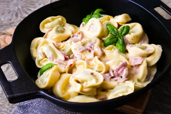 Frische Tortellini mit Schinken in cremiger Sauce, garniert mit Basilikum. Ein Genuss, wenn man Tortellini selber machen möchte.