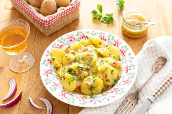 Salade de pommes de terre avec oignons rouges et persil, servie dans une assiette fleurie.