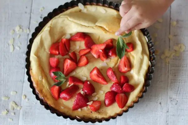 Puszysty dutch baby z truskawkami i płatkami migdałów, dekorowany przez dziecko.