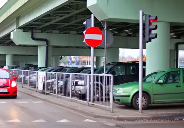 Czerwony samochód zbliża się do parkingu, gdzie stoi znak b2. Zielony samochód zaparkowany jest pod wiaduktem.