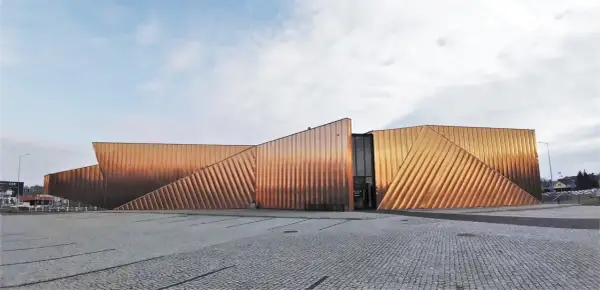 Nowoczesny budynek muzeum ognia z miedzianą elewacją, przypominającą płomienie.