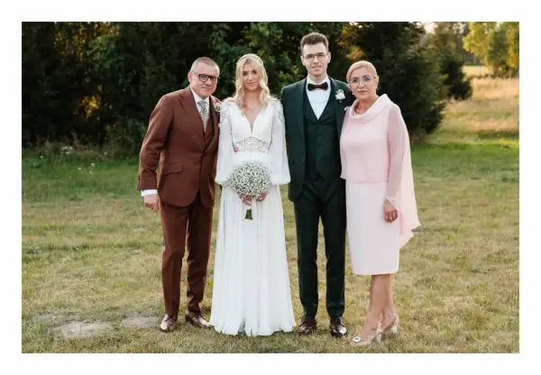 Rodzice i para młoda elegancko na ślub córki. Ojciec w brązowym garniturze, matka w różowej sukience.