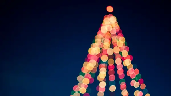 Luci natalizie sfocate creano la forma di un albero su sfondo blu scuro.