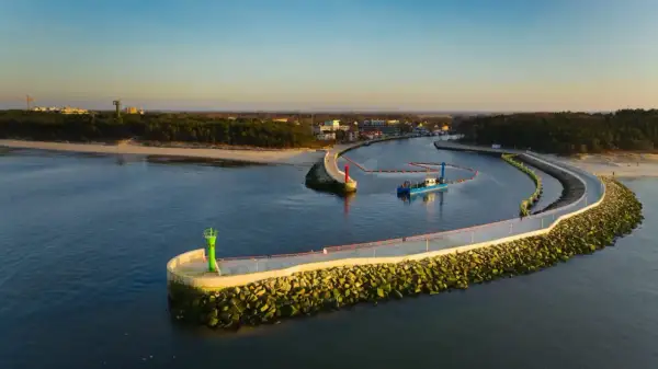 Port w Mrzeżynie z falochronami i latarniami morskimi. Widoczna łódź pogłębiarka. To jedne z mrzeżyno atrakcje.