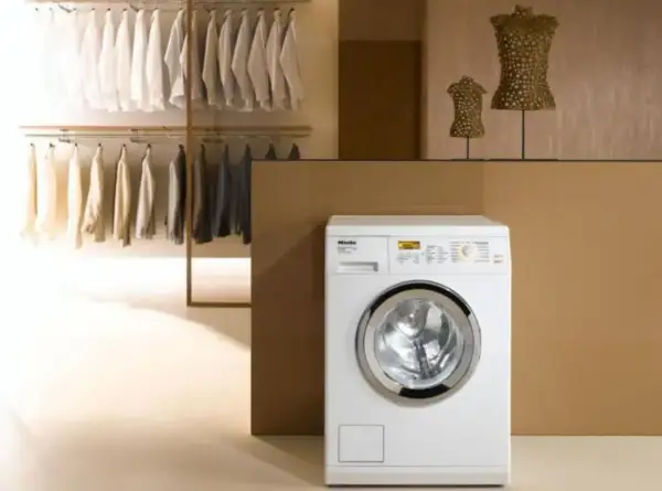 Lavatrice Miele bianca con ingresso acqua calda e fredda, accanto a un armadio con abiti ordinati.