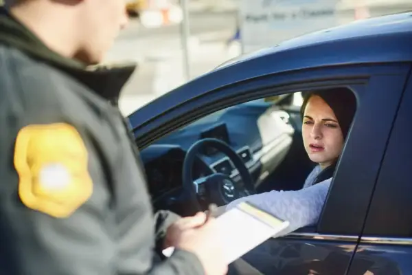 Policjant wręcza kobiecie w samochodzie dokumenty. Wygląda na to, że chodzi o mandaty w Austrii.