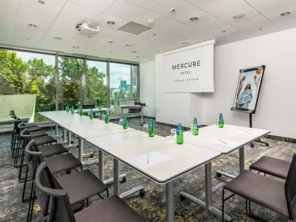 Sala konferencyjna w hotelu Mercure Poznań Centrum gotowa na spotkanie. Stoły ustawione, woda czeka, a za oknem zieleń.