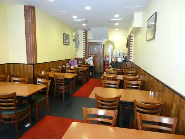 Interiör av en turkisk restaurang i Stockholm. Flera bord med trästolar och röda mattor. Tre gäster sitter vid borden.